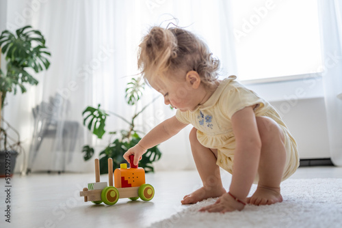Two years old child boy playing with wooden colourful train at home. Educational eco-friendly toys concept. Development of kids fine motor skills, imagination and logical thinking