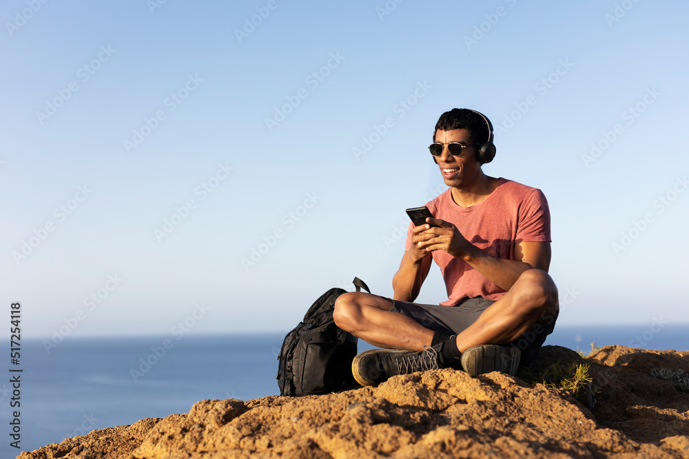 Young man sitting on the stone listening the music. Tourist man on the top of the mountain...