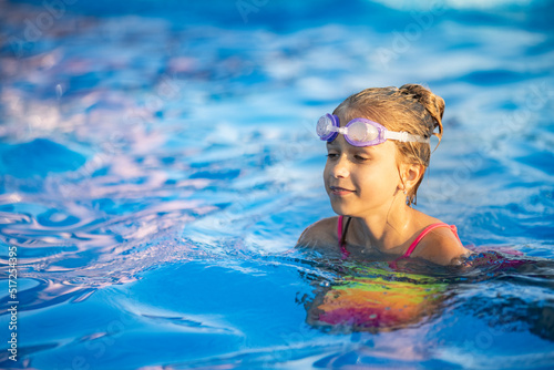 A girl in a bright bathing suit swims with an inflatable ball in a pool with clear water on a summer evening