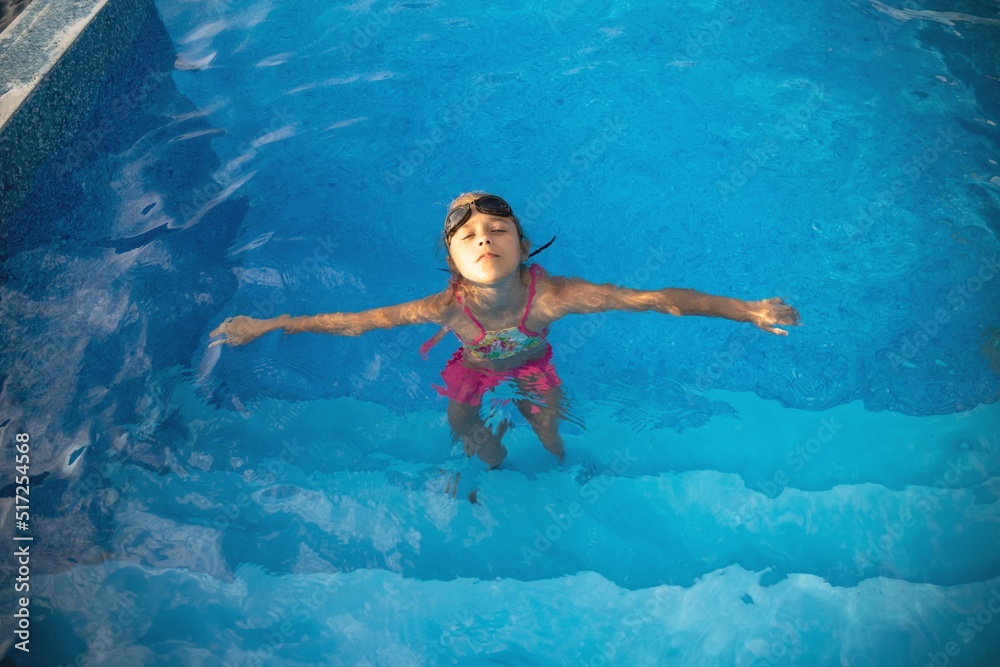 A girl in a bright swimsuit with swimming goggles dives into a pool with clear transparent water