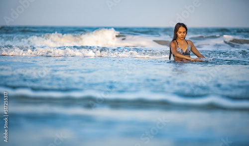 Girl with wet hair in a leopard swimsuit splashes water while sitting in the sea © YouraPechkin