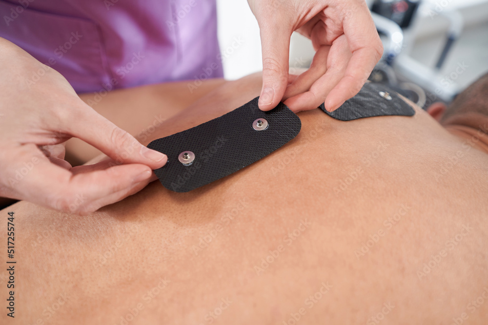 Doctor hands placing myostimulation electro pads on male back Doctor hands placing myostimulation electro pads on male back