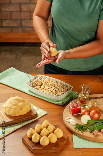 Woman hands preparing brazilian croquette (coxinha de frango) on a wooden table.