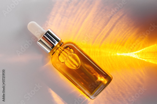 Mockup of glass dropper bottle with a metal cap and yellow essential oil on a background with an abstract fire pattern of light and shadow. Eco cream, serum, cosmetics, massage oil. Copy space