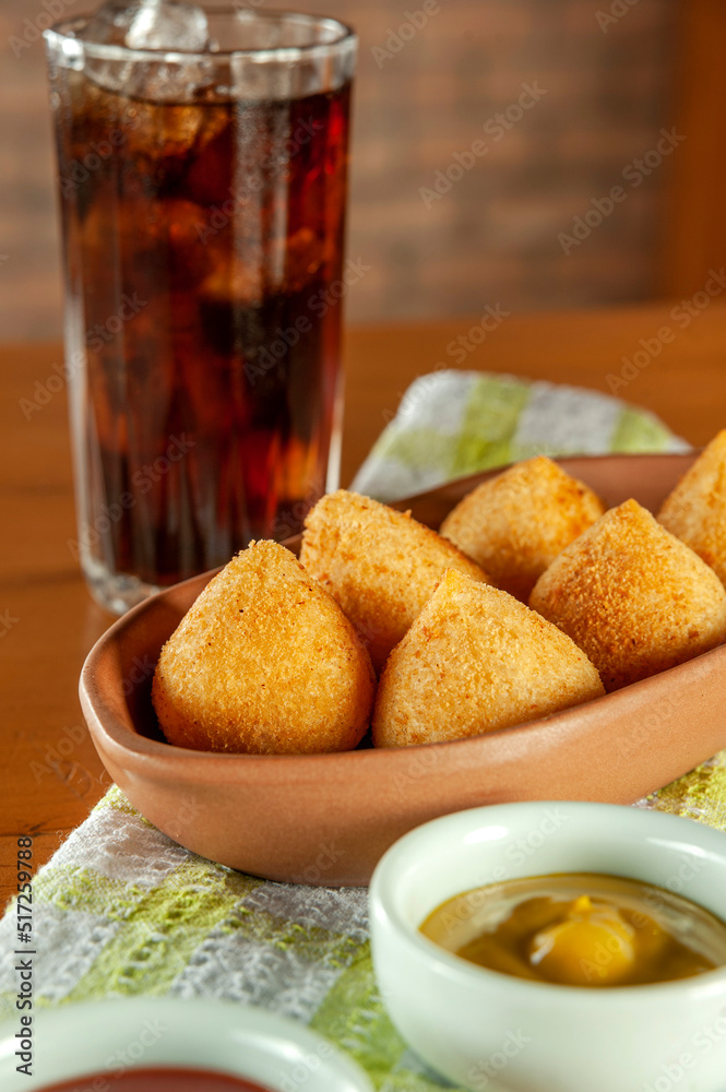 Fried brazilian croquettes (coxinha de frango) with iced soda in a kitchen with bricks wall. Fried brazilian croquettes (coxinha de frango) with iced soda in a kitchen with bricks wall.