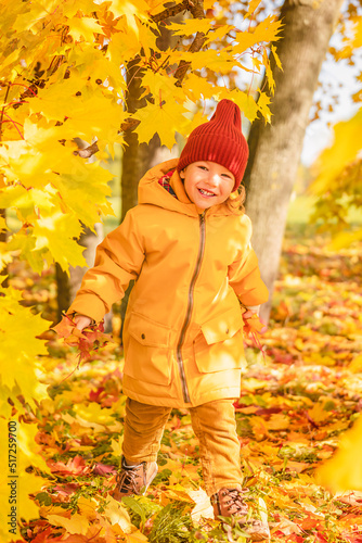 Beautiful little child girl walking with maple leaves in the autumn park. Happy child girl having fun in autumn park