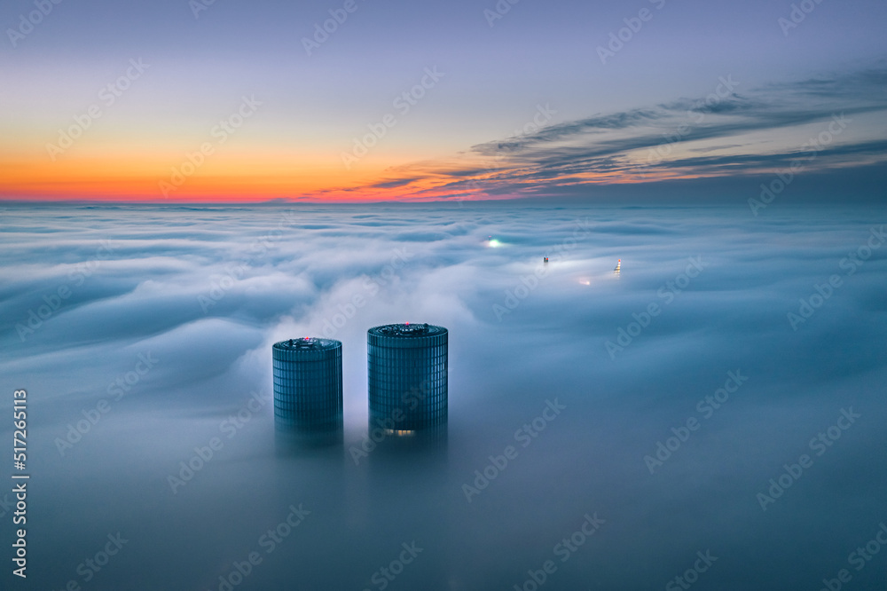 Skyscraper rooftop over the clouds at sunrise. Thick fog covers the Riga city, and warm sunlight over the clouds.
