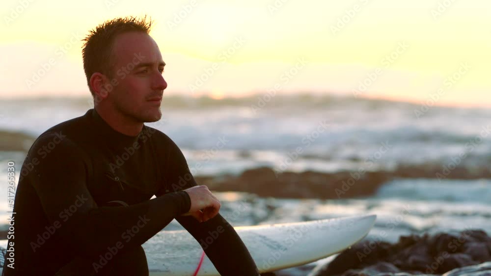 Man surfing on the beach at sunset, enjoying the view and relaxing. Surfer guy sitting and thinking calm thoughts, taking a break from sport and dreaming about his wellness goals Man surfing on the beach at sunset, enjoying the view and relaxing. Surfer guy sitting and thinking calm thoughts, taking a break from sport and dreaming about his wellness goals