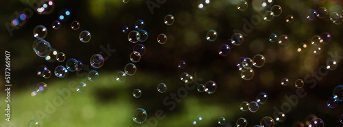 Banner. Festive background with shimmering shiny iridescent transparent soap bubbles on the green grass. Beautiful bokeh.