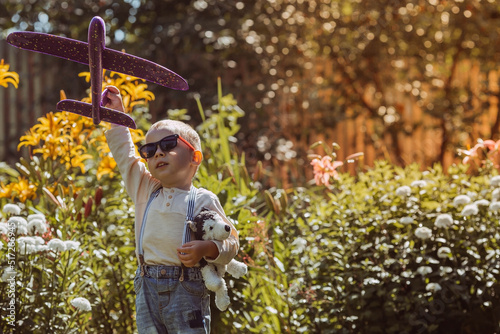 A little boy in sunglasses launches a toy airplane in nature. Summer time, happy childhood, dreams and carelessness. Air tour. Fly on a trip, flight, adventure and vacation. photo