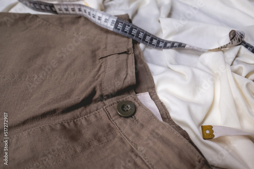 Belt and label detail of fashion cotton dark khaki shorts over wrinkled white sheet with vinyl measure tape