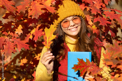 Autumn teen child girl portrait, fall leaves concept. cheerful kid hold book on autumn leaves background