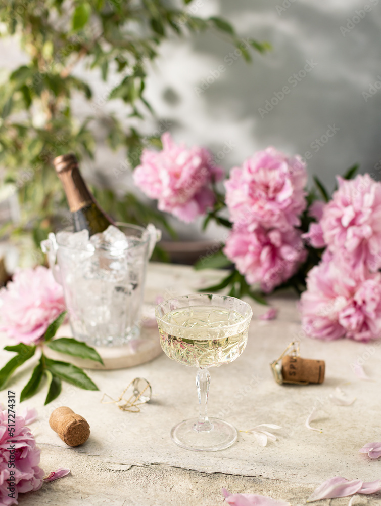 Glass of champagne on concrete grey background with bucket of ice and a bottle of champagne and purple peonies.romantic card.