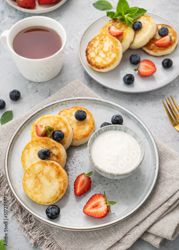 cheesecakes or cottage cheese or syrniki with fresh blerries and sour cream on a gray background with a cup of tea. The concept of a healthy and delicious breakfast. Vertical orientation