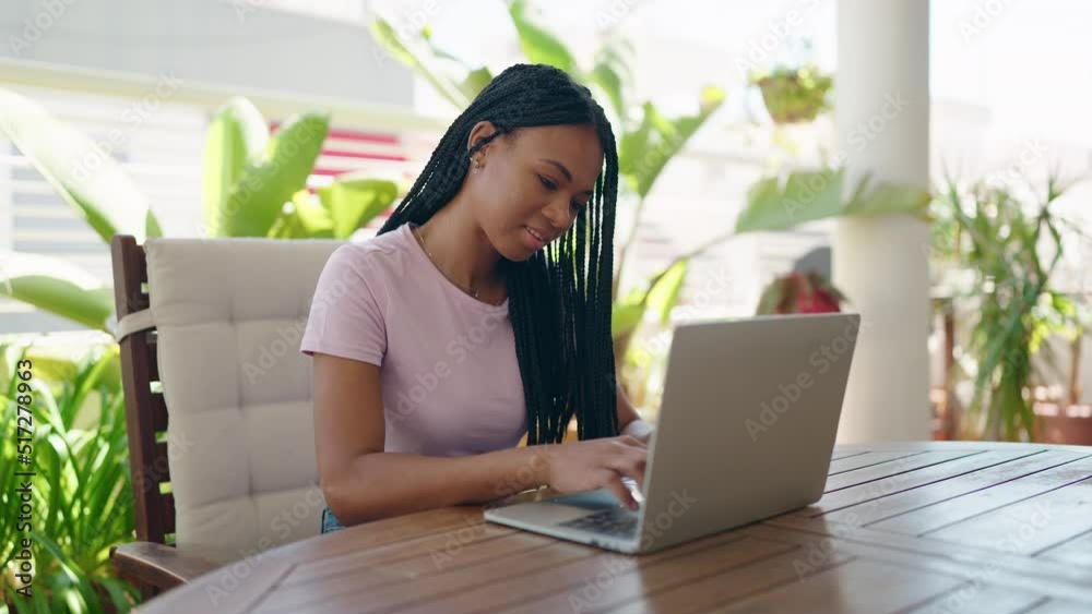 African american woman using laptop sitting on table at home terrace African american woman using laptop sitting on table at home terrace