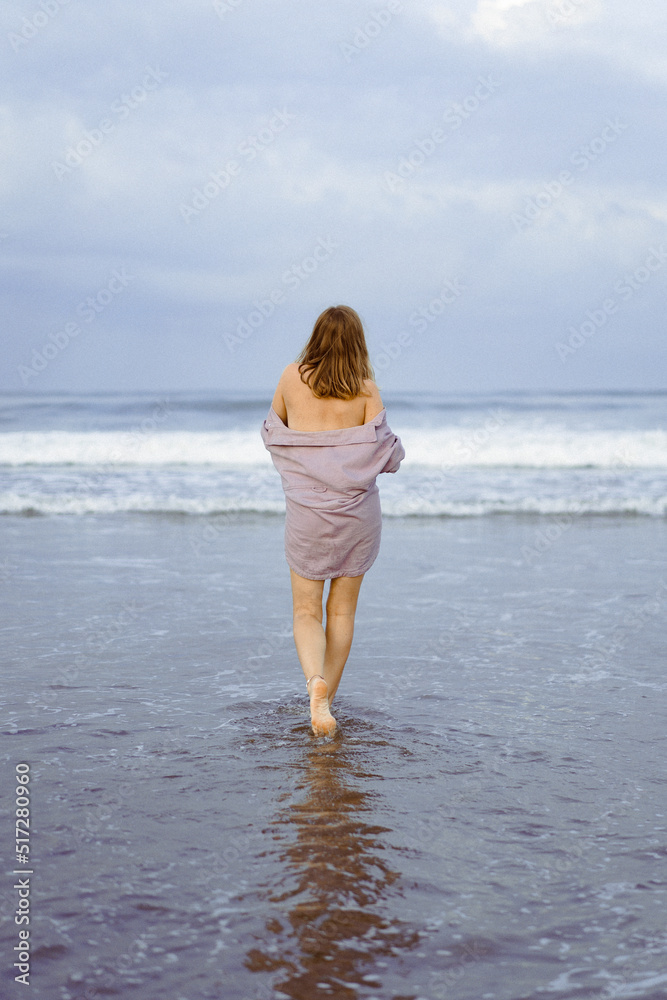 A young woman walks along the ocean at dawn, a time of meditation and reflection.
