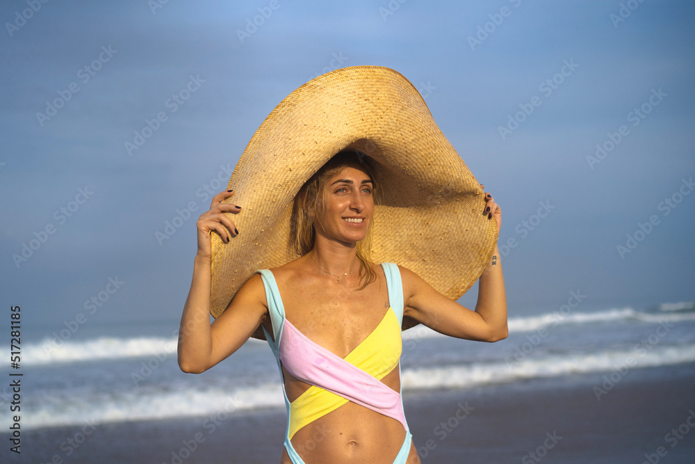 Young attractive woman in a big straw hat on the beach near the ocean. .Walk along the beach, have fun, vacation by the sea.