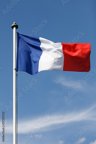French flag flying in the wind with blue sky background.  Flag of France, the Tricolor on a White flagpole,