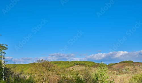 Scenic landscape of a peaceful meadow with dark clouds in a blue sky background and copy space. Calm and tranquil view of blooming lush plants on a hill in the countryside or wilderness in nature