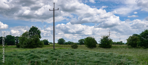 krajobraz linii elektrycznej pośrodku zielonych pól w zachodniej Polsce, jasne zielono niebieskie kolory lekko pochmurna pogoda