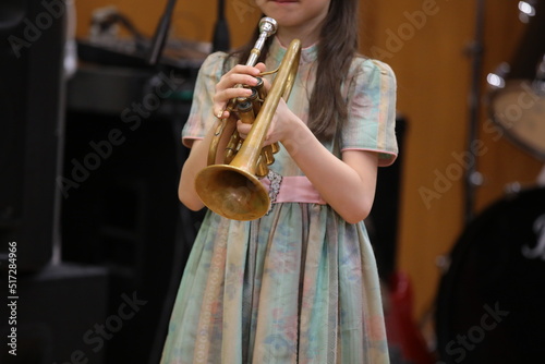 A little girl young musician trumpeter playing trumpet concert standing on stage alone holding professional musical instrument in hand