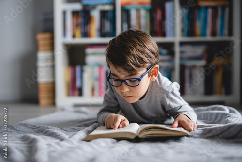 One caucasian boy lying on the floor at home in day reading a book front view wearing eyeglasses copy space real people photo