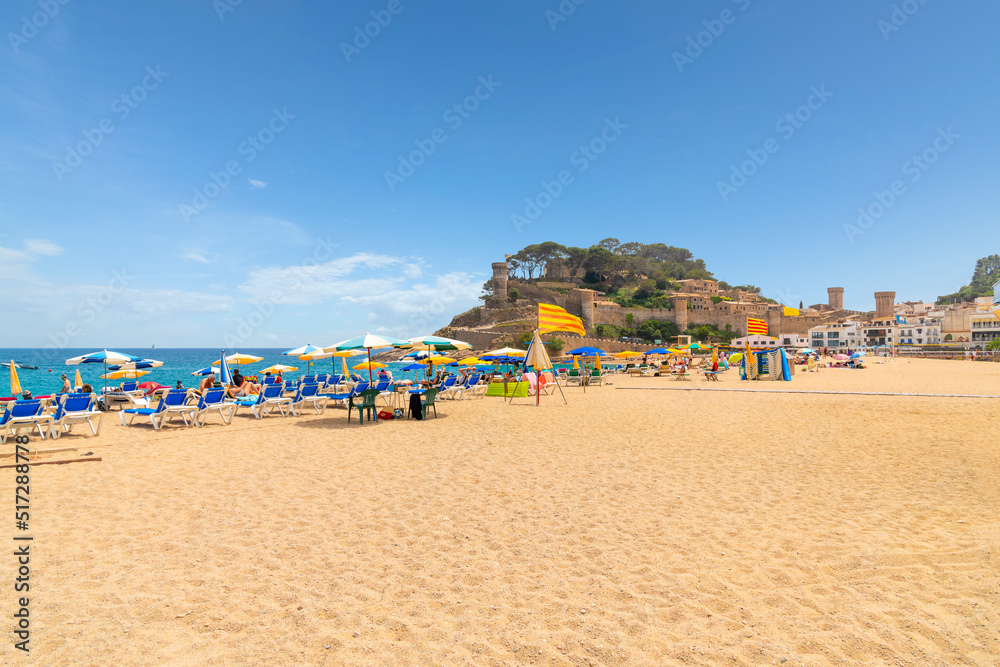 Spanish and tourists enjoy a sunny summer day at Platja Gran, the wide sandy beach at the Costa Brava town of Tossa de Mar with the 12th century Castle in view behind.