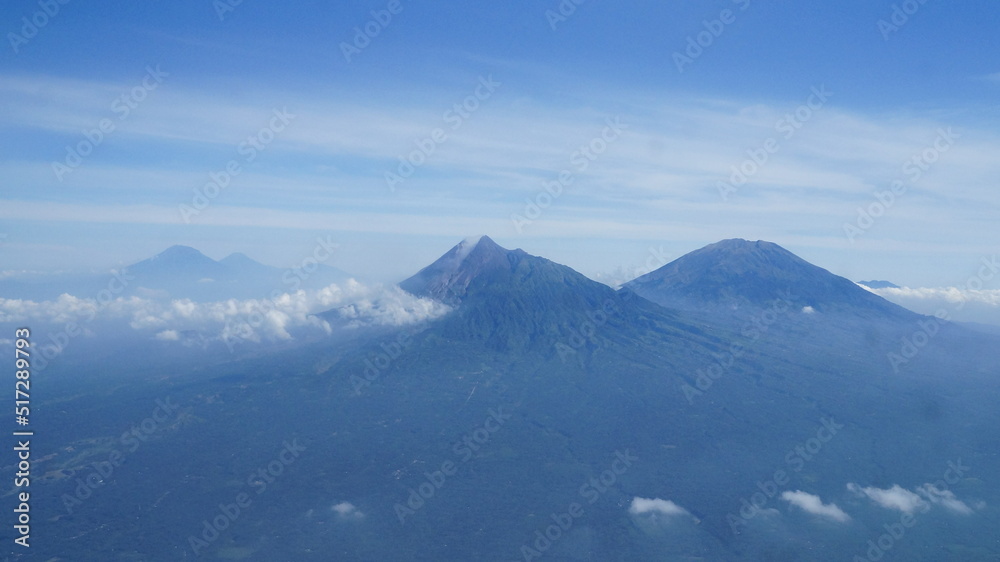 an aerial view of two mountains in Yogyakarta and Central Java, Indonesia. The left mountain is Mount Merapi, the most active volcano in Indonesia and the right one is Mount Merbabu