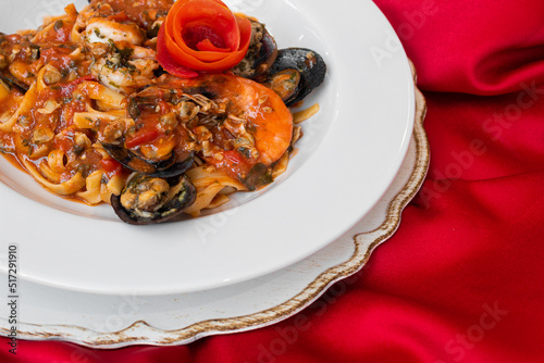 Massa fettuccine com molho de frutos-do-mar, mediterrâneo com flor de tomate em prato branco e toalha vermelha tipico italiano © Felipe Mota