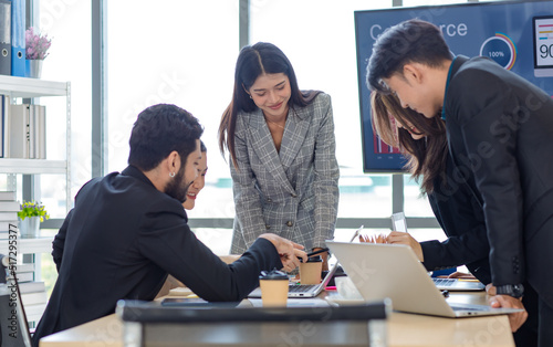 Businesswoman manager presenter in formal suit standing holding pen pointing at graph chart document on whiteboard presenting company information to Asian male female colleagues in meeting room