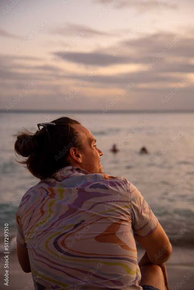 One man sitting on a beach with sunset sky in background at golden hour. One man sitting on a beach with sunset sky in background at golden hour.