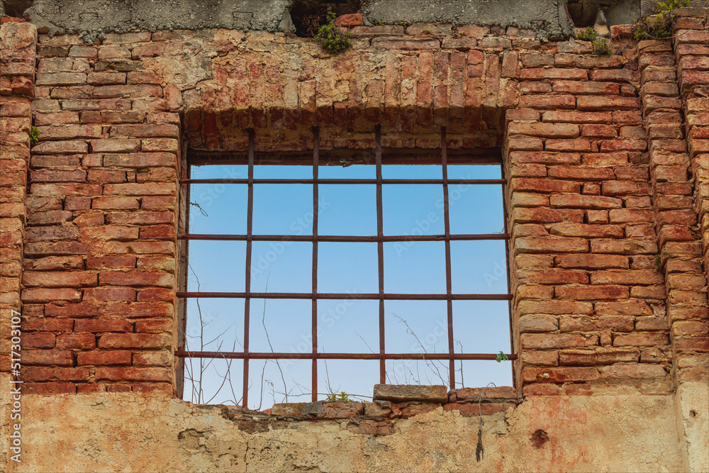 Vecchia finestra, che guarda sul cielo azzurro, sbarrata e su muro rosso di mattoni di vecchio edificio.