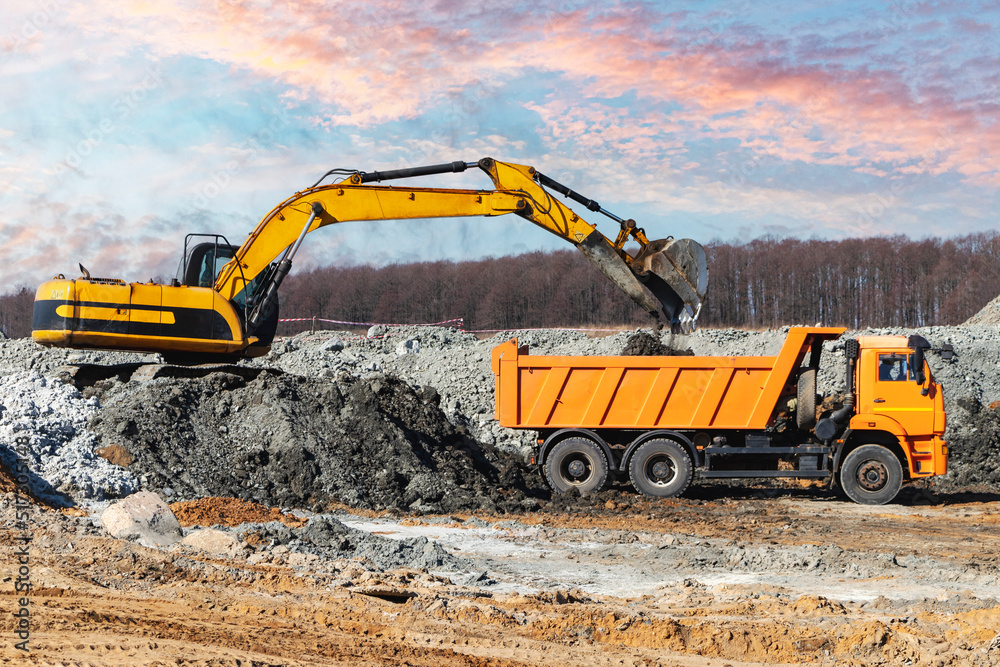 A powerful crawler excavator loads the earth into a dump truck against the blue sky. Development and removal of soil from the construction site. A powerful crawler excavator loads the earth into a dump truck against the blue sky. Development and removal of soil from the construction site.
