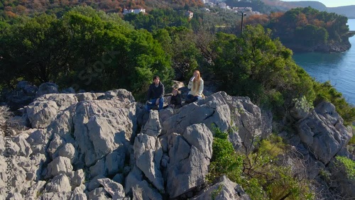 A family of tourists father, mother and son are shooting a selfie video on a drone. They are sitting on a rock above the Queen's beach near the city of Budva. Travel to Montenegro concept photo