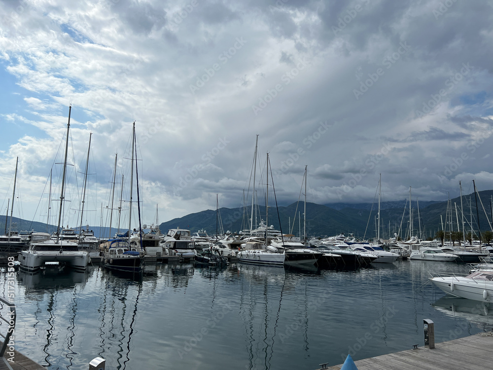 Sailing yachts stand at the pier against the backdrop of the mountains
