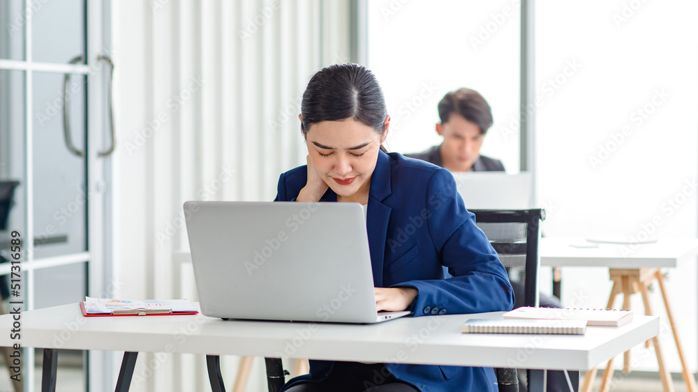 Asian stressed exhausted tired female businesswoman secretary working late and hard sitting at workplace in company take off glasses hold hand massaging painful shoulder from office syndrome symptom