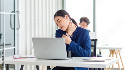 Asian stressed exhausted tired female businesswoman secretary working late and hard sitting at workplace in company take off glasses hold hand massaging painful shoulder from office syndrome symptom
