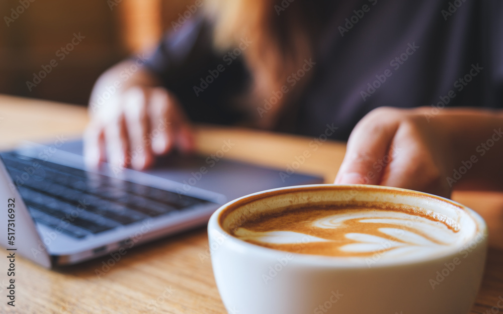 Closeup image of a woman holding and drinking hot coffee while working on laptop computer Closeup image of a woman holding and drinking hot coffee while working on laptop computer