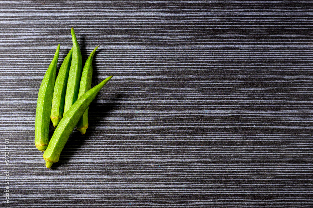 Fresh Ochra, Bhindi or Ladies Fingers whole and uncooked against a grey horizontal stripped background Fresh Ochra, Bhindi or Ladies Fingers whole and uncooked against a grey horizontal stripped background