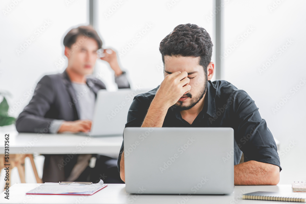 Indian stressed depressed exhausted bearded male businessman sitting at workstation with laptop computer close eyes hold hand on head feeling tired and sleepy after working late overtime last night