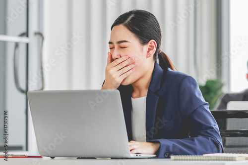 Closeup shot of millennial Asian young stressed depressed sleepy female businesswoman employee sitting holding hand on messy hair working on workstation desk via laptop notebook computer in office