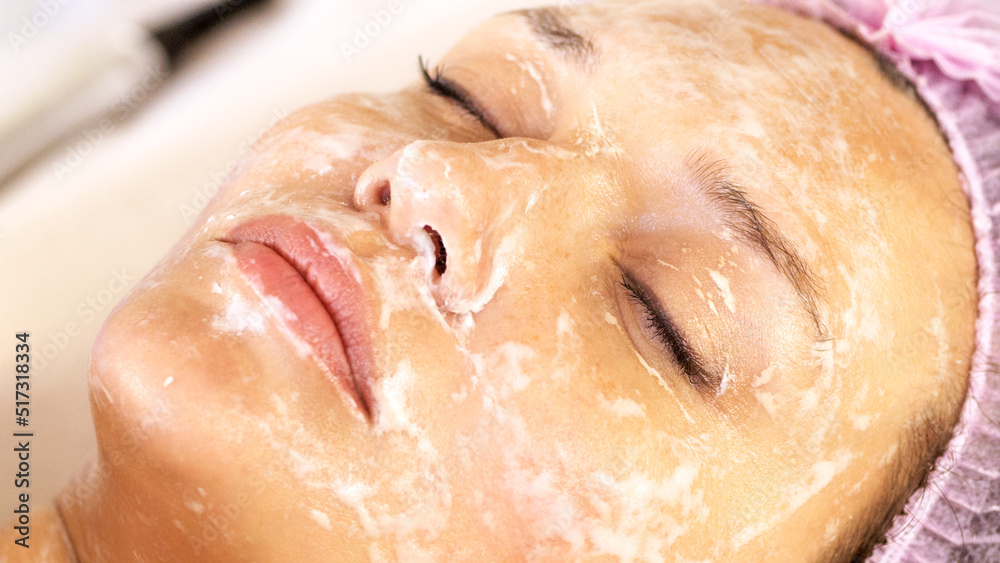 Cosmetologist applies  a moisturizing mask on female face. Woman in a spa salon on cosmetic procedures for facial care.  White woman getting beauty treatment therapy.