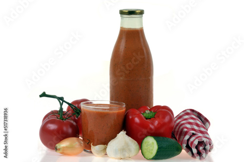 Bouteille et verre de gaspacho maison avec ses ingrédients sur fond blanc