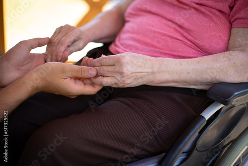 gros plan sur les mains d'une personne âgée en fauteuil roulant tenant celles d'un jeune homme. Symbole de la compassion et de la solidarité 