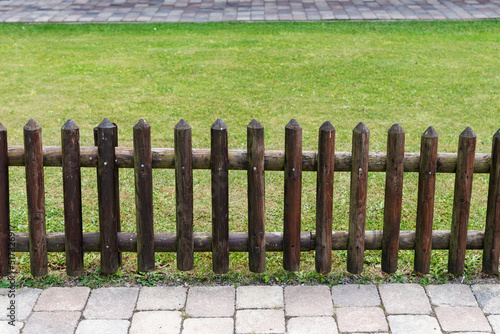 A small wooden fence separates the sidewalk and the lawned garden photo