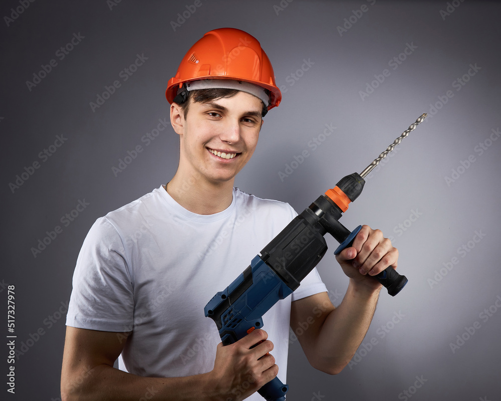 a young construction worker in a hard hat and a white T-shirt with a puncher in his hand. a young construction worker in a hard hat and a white T-shirt with a puncher in his hand.