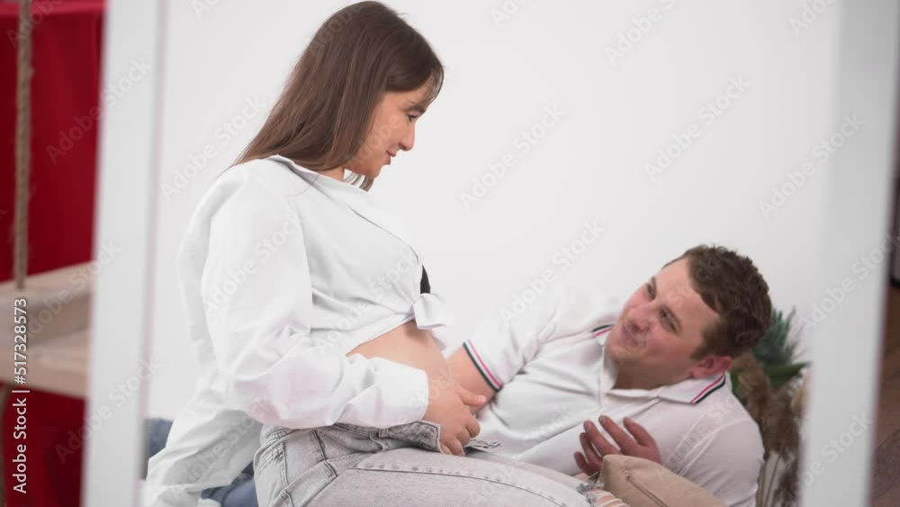 Young expectant mother caresses her belly. Pregnant young woman with husband expecting a baby. Happy pregnant woman with big belly resting at home. The young family is waiting for replenishment. Young expectant mother caresses her belly. Pregnant young woman with husband expecting a baby. Happy pregnant woman with big belly resting at home. The young family is waiting for replenishment.