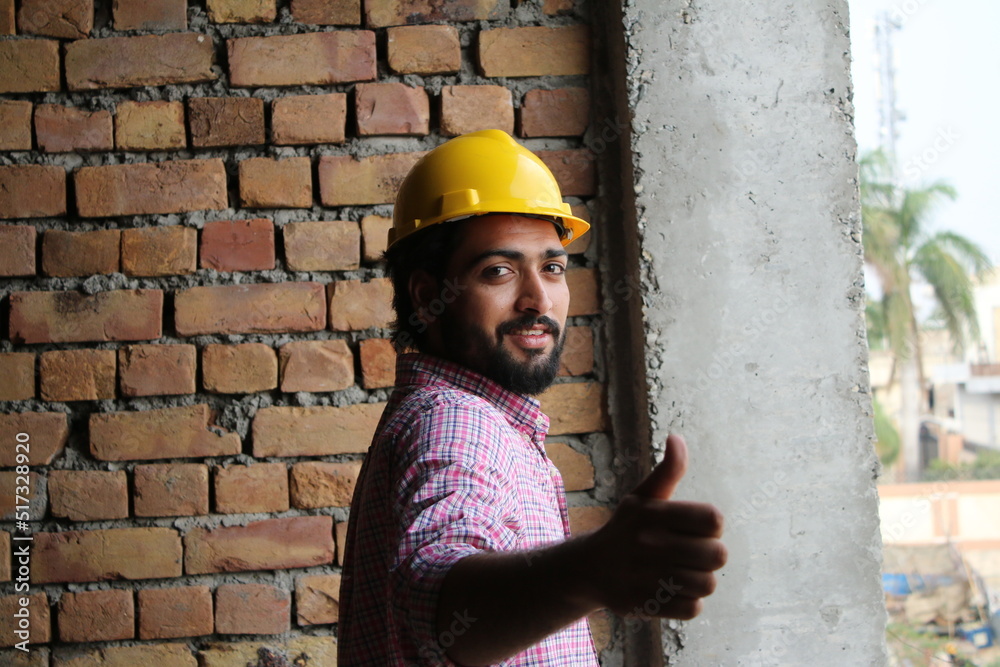 Young engineer wearing yellow safety helmet standing on construction site in happy mood