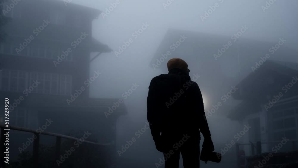 Back view of a man with a backpack in a thick fog. Concept of a ghost town or a horror movie vibes. Back view of a man with a backpack in a thick fog. Concept of a ghost town or a horror movie vibes.