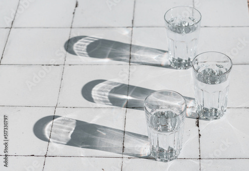 glass with clean clear water and sharp shadows stands on a white wood table. top view of glass with water on white tableon a tiled table photo